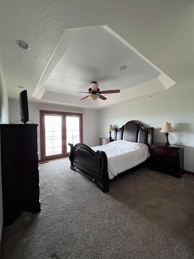 carpeted bedroom featuring a textured ceiling, ceiling fan, and a raised ceiling