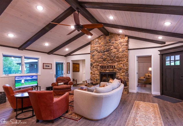 living room featuring ceiling fan, lofted ceiling with beams, wood-type flooring, and a stone fireplace