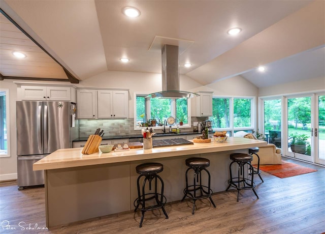 kitchen with lofted ceiling, a kitchen breakfast bar, island range hood, and stainless steel refrigerator