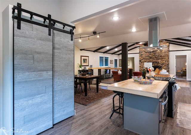 kitchen featuring a fireplace, gas stove, island range hood, hardwood / wood-style flooring, and lofted ceiling with beams