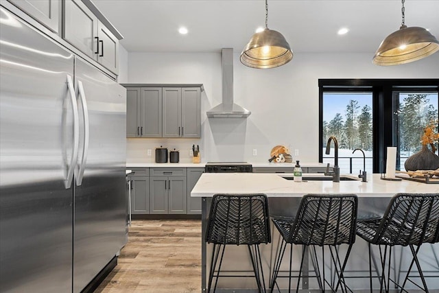 kitchen featuring built in fridge, gray cabinets, stove, wall chimney range hood, and a kitchen breakfast bar