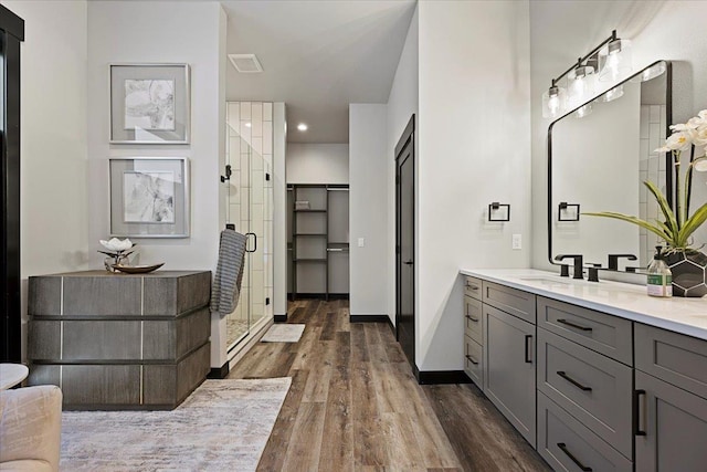 bathroom with wood finished floors, visible vents, vanity, baseboards, and a shower stall