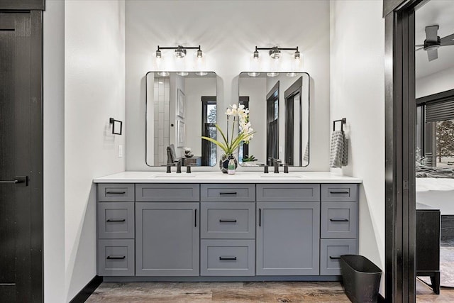 full bath with double vanity, wood finished floors, a sink, and a ceiling fan