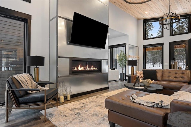 living area with wooden ceiling, a high ceiling, an inviting chandelier, wood finished floors, and a warm lit fireplace