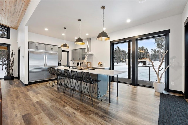 kitchen with built in fridge, light countertops, gray cabinetry, a sink, and wall chimney exhaust hood