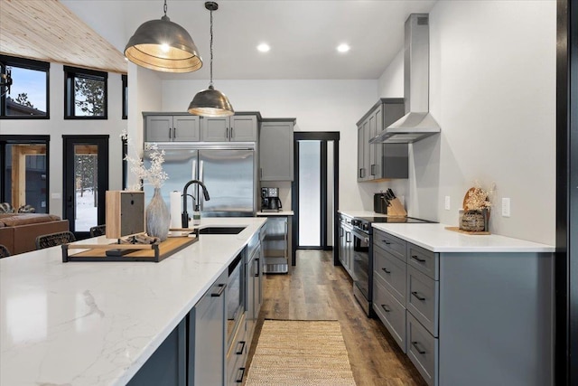 kitchen with wall chimney exhaust hood, light stone counters, wood finished floors, stainless steel appliances, and gray cabinetry