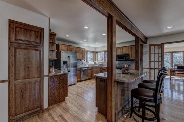 kitchen featuring dark stone countertops, appliances with stainless steel finishes, tasteful backsplash, and light wood-type flooring