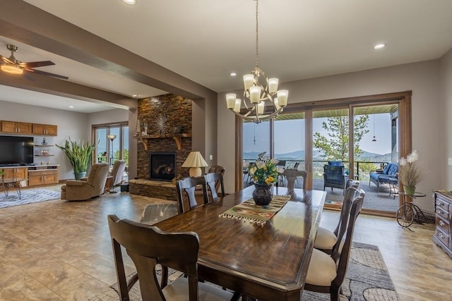 tiled dining area with a stone fireplace, a healthy amount of sunlight, and ceiling fan with notable chandelier