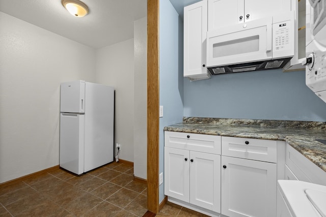 kitchen with white appliances, dark stone counters, white cabinetry, and dark tile floors