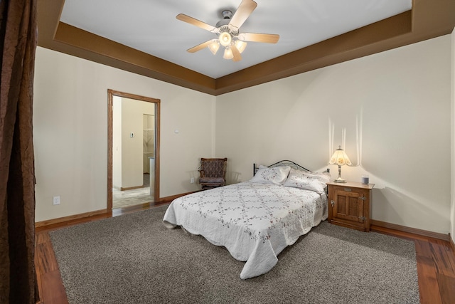 bedroom featuring a raised ceiling, ceiling fan, and dark wood-type flooring