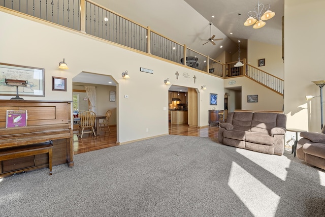 living room with high vaulted ceiling, carpet flooring, and ceiling fan with notable chandelier