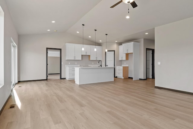 kitchen with white cabinetry, sink, hanging light fixtures, a kitchen island with sink, and light wood-type flooring