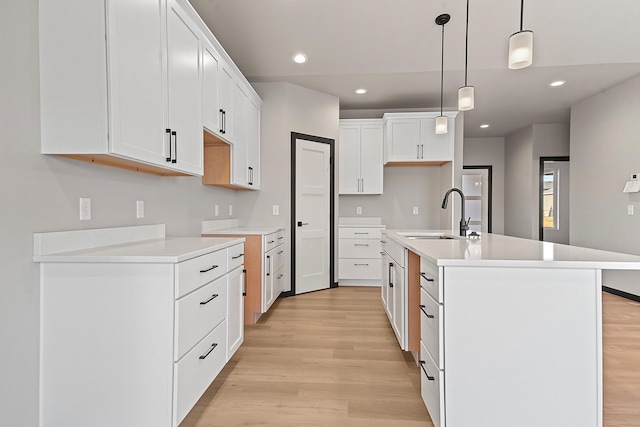 kitchen featuring an island with sink, sink, white cabinets, hanging light fixtures, and light hardwood / wood-style flooring