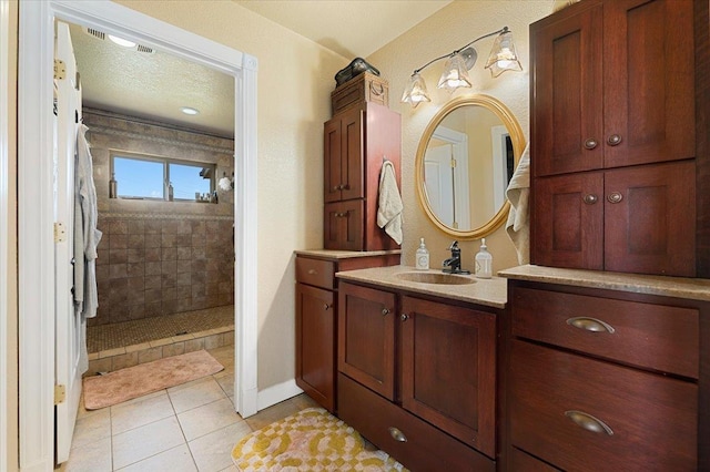 bathroom with tile patterned floors, vanity, tiled shower, and a textured ceiling