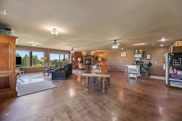 living room with ceiling fan, a fireplace, concrete floors, and a textured ceiling