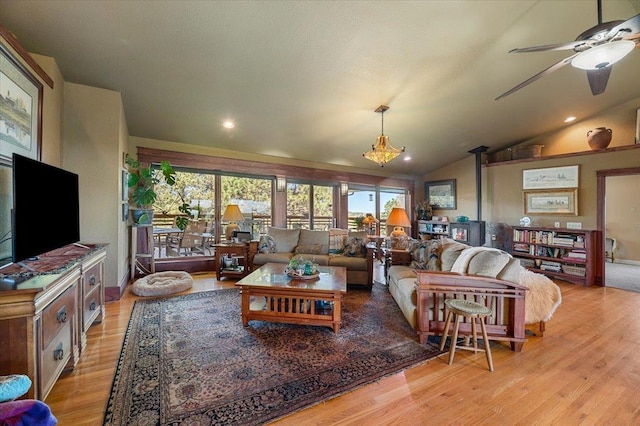 living room featuring a wood stove, ceiling fan, vaulted ceiling, and light wood-type flooring