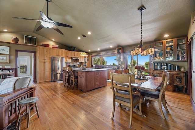 dining area featuring ceiling fan with notable chandelier, light wood-type flooring, a textured ceiling, and vaulted ceiling