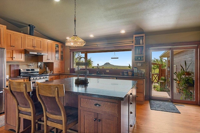 kitchen featuring light hardwood / wood-style flooring, a textured ceiling, vaulted ceiling, a kitchen island, and appliances with stainless steel finishes