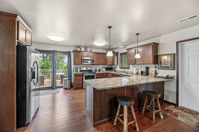 kitchen with light stone countertops, hanging light fixtures, dark hardwood / wood-style floors, kitchen peninsula, and appliances with stainless steel finishes