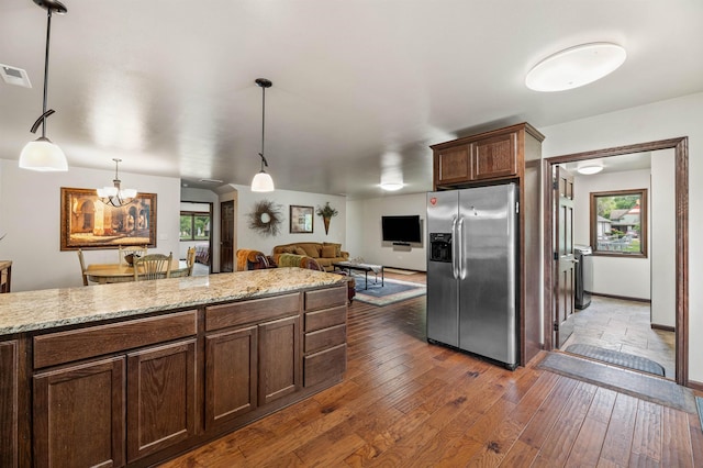 kitchen with dark hardwood / wood-style floors, stainless steel fridge with ice dispenser, light stone counters, and decorative light fixtures