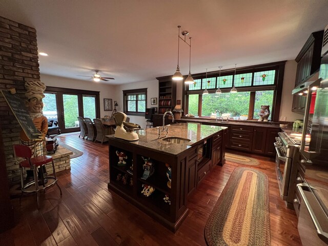 kitchen with an island with sink, sink, dark wood-type flooring, and light stone counters