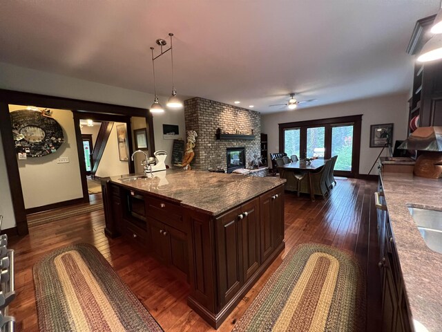 kitchen with light stone countertops, a fireplace, dark wood-type flooring, hanging light fixtures, and ceiling fan