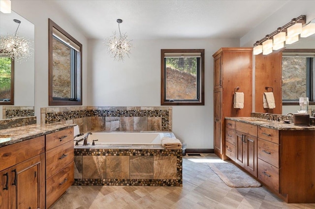 bathroom featuring an inviting chandelier, vanity, and tiled tub