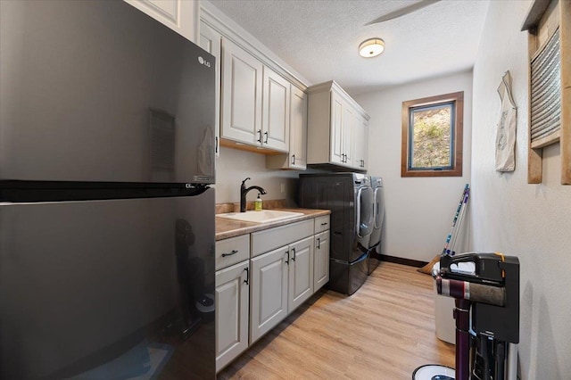 laundry area featuring washer and clothes dryer, sink, cabinets, light wood-type flooring, and a textured ceiling