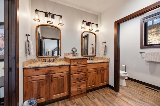 bathroom featuring toilet, hardwood / wood-style flooring, and dual bowl vanity