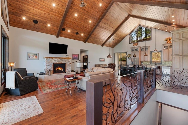 living room with wood-type flooring, wooden ceiling, high vaulted ceiling, beamed ceiling, and a stone fireplace