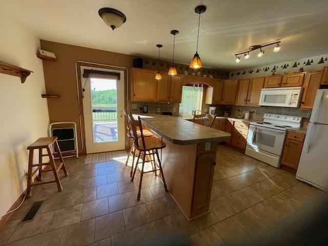 kitchen featuring decorative backsplash, a kitchen breakfast bar, white appliances, pendant lighting, and a kitchen island