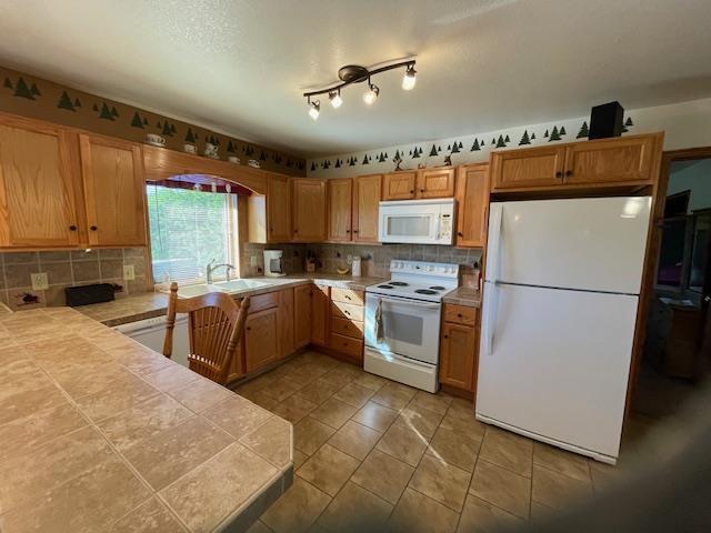 kitchen with backsplash, white appliances, sink, tile countertops, and tile patterned flooring