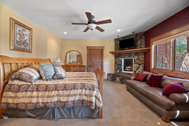 carpeted bedroom featuring a stone fireplace and ceiling fan