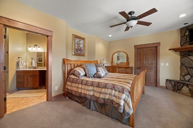 bedroom with a stone fireplace, connected bathroom, carpet floors, and ceiling fan