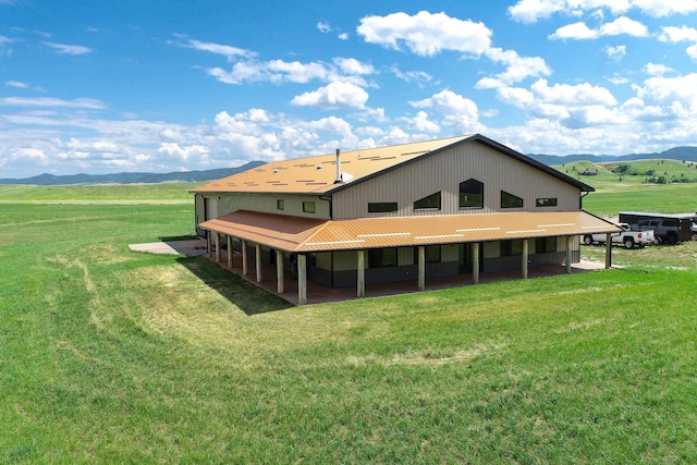 rear view of property with a mountain view, a rural view, an outbuilding, and a lawn