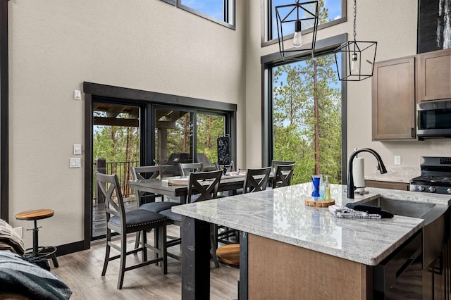 kitchen featuring range with gas cooktop, decorative light fixtures, a high ceiling, light wood-type flooring, and light stone countertops