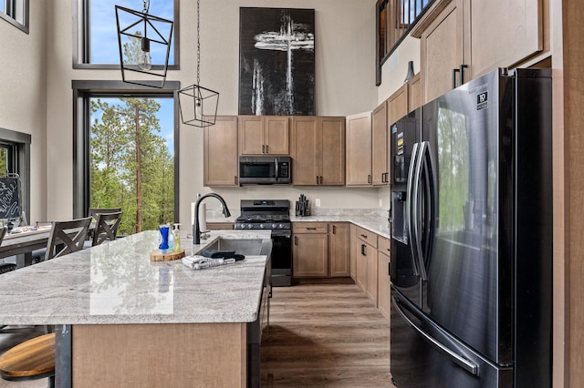 kitchen with decorative light fixtures, a center island with sink, dark hardwood / wood-style floors, appliances with stainless steel finishes, and a towering ceiling