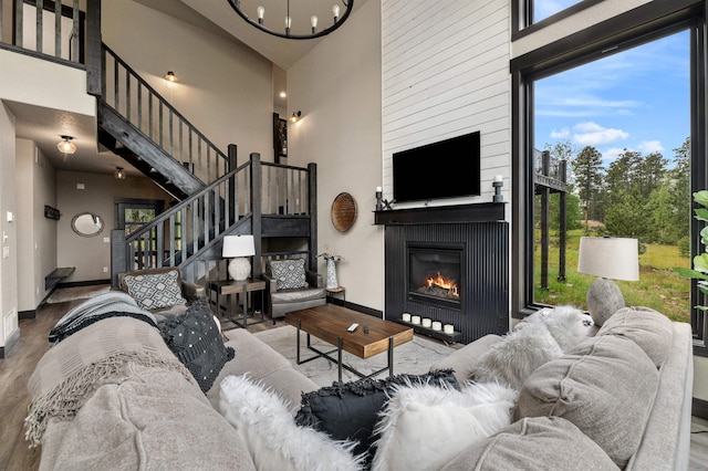 living room featuring a chandelier, wood-type flooring, a towering ceiling, and a large fireplace