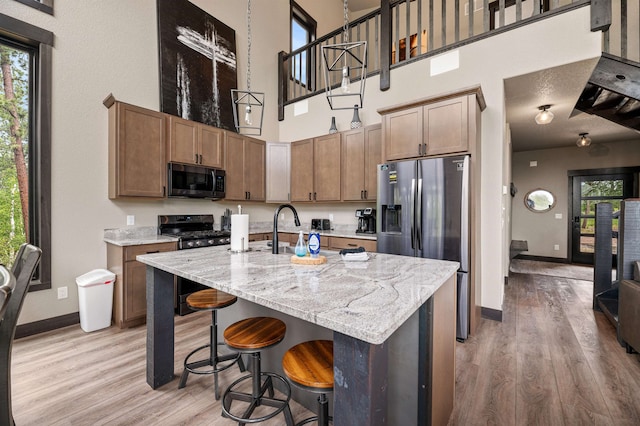 kitchen featuring gas range, an island with sink, light stone countertops, light hardwood / wood-style flooring, and a towering ceiling