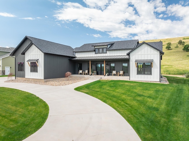 exterior space featuring board and batten siding, a shingled roof, a standing seam roof, and a front yard