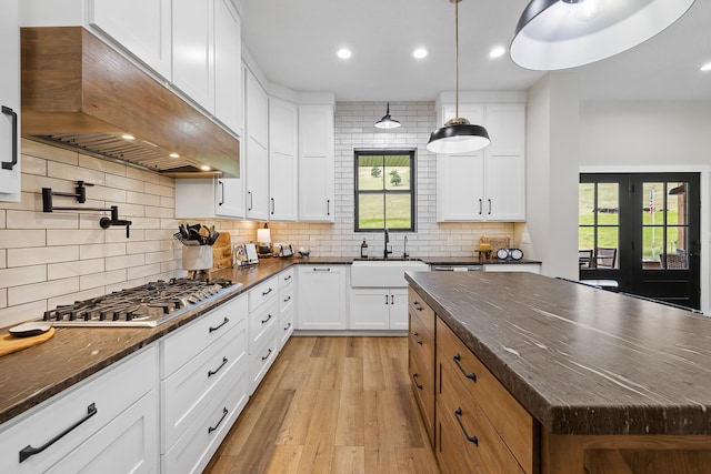 kitchen featuring custom range hood, dark stone countertops, stainless steel gas stovetop, white cabinets, and a sink