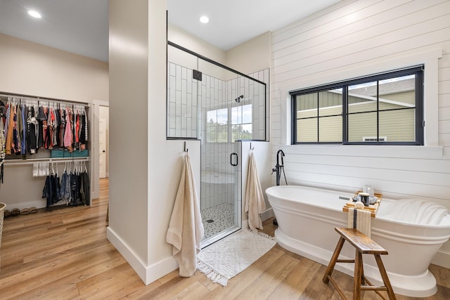 bathroom with a walk in closet, a soaking tub, wood finished floors, and a stall shower