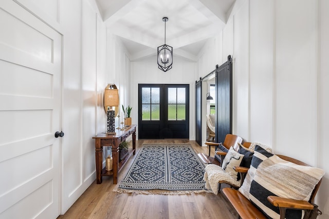 foyer entrance featuring a barn door, vaulted ceiling, an inviting chandelier, wood finished floors, and a decorative wall