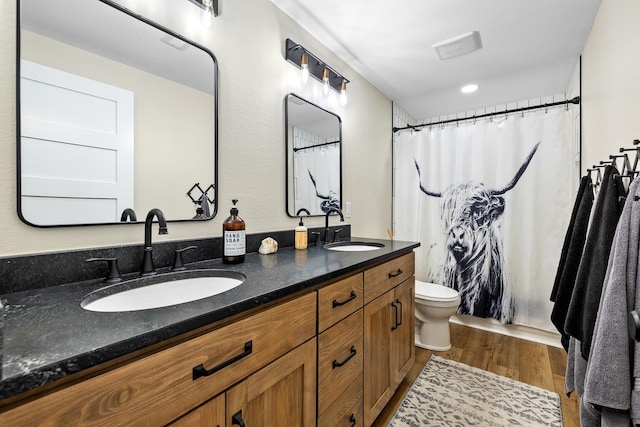 full bathroom with double vanity, toilet, wood finished floors, and a sink