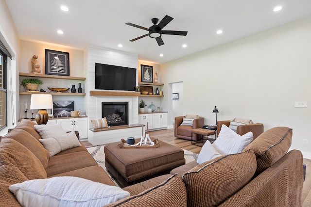 living room with ceiling fan, light hardwood / wood-style floors, and a large fireplace