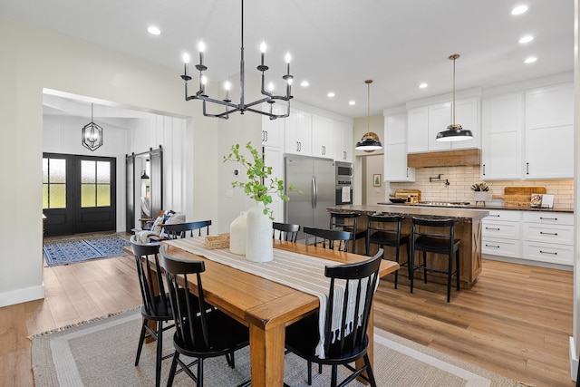 dining area with light hardwood / wood-style floors, french doors, and an inviting chandelier