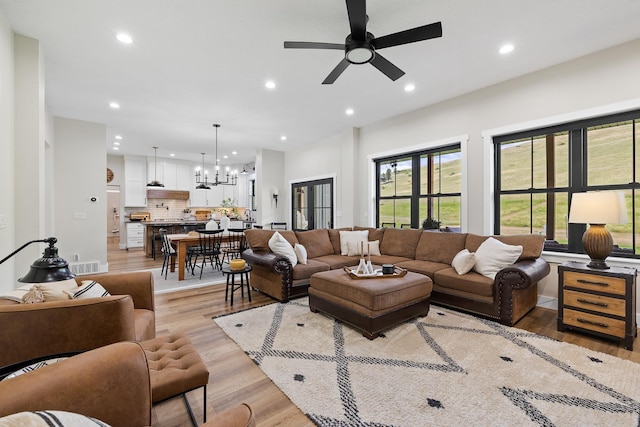 living room with ceiling fan with notable chandelier, light wood-style flooring, and recessed lighting