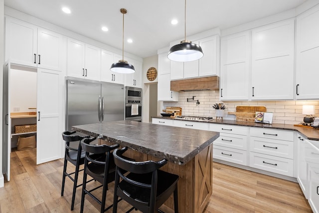 kitchen with hanging light fixtures, decorative backsplash, a center island, a kitchen bar, and light hardwood / wood-style flooring