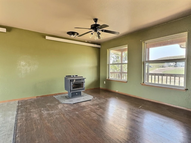 unfurnished living room featuring ceiling fan, dark hardwood / wood-style flooring, and a wood stove