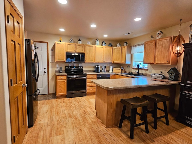 kitchen featuring a breakfast bar area, black appliances, sink, kitchen peninsula, and light wood-type flooring